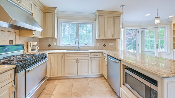 A modern kitchen with beige cabinetry, a stainless steel range hood, a built-in oven, and a large window providing natural light. - Private Pool & Patio: Luxe Westchester Home! (Briarcliff Manor)