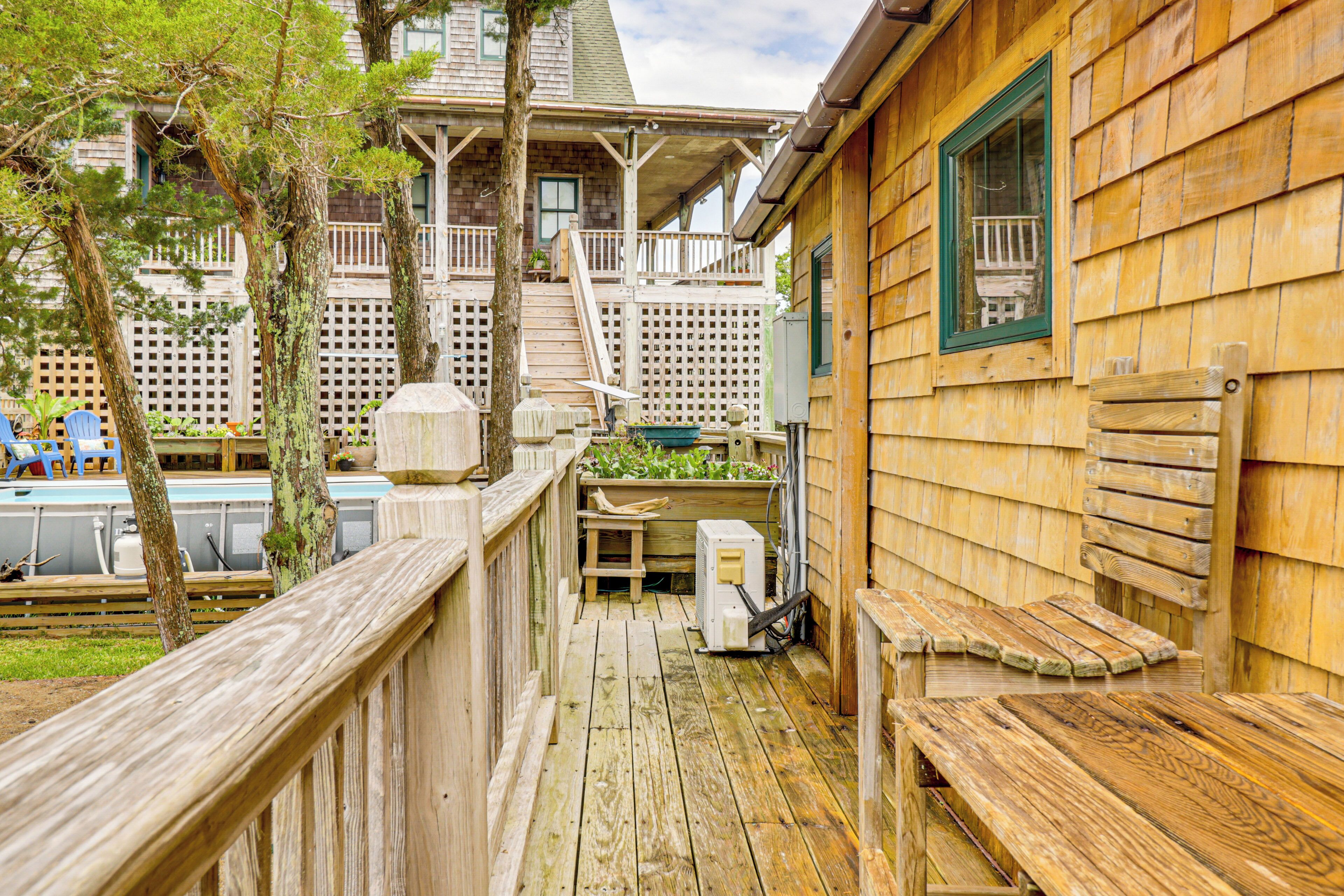 Une terrasse en bois avec un banc en bois et une petite table, une clôture en bois et une vue sur un b âtiment doté d’un porche et d’un escalier.