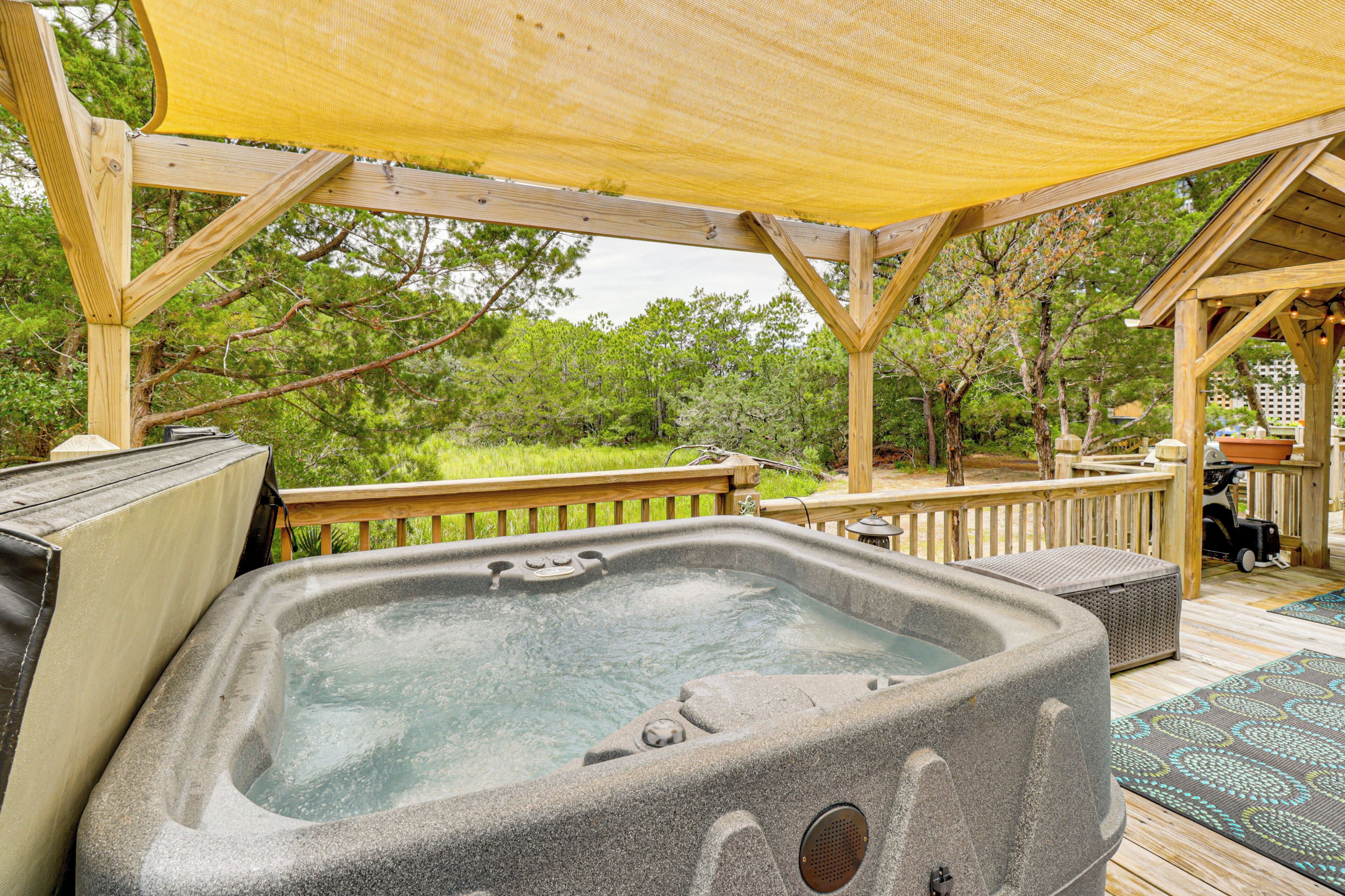 A hot tub under a wooden pergola with a view of trees.