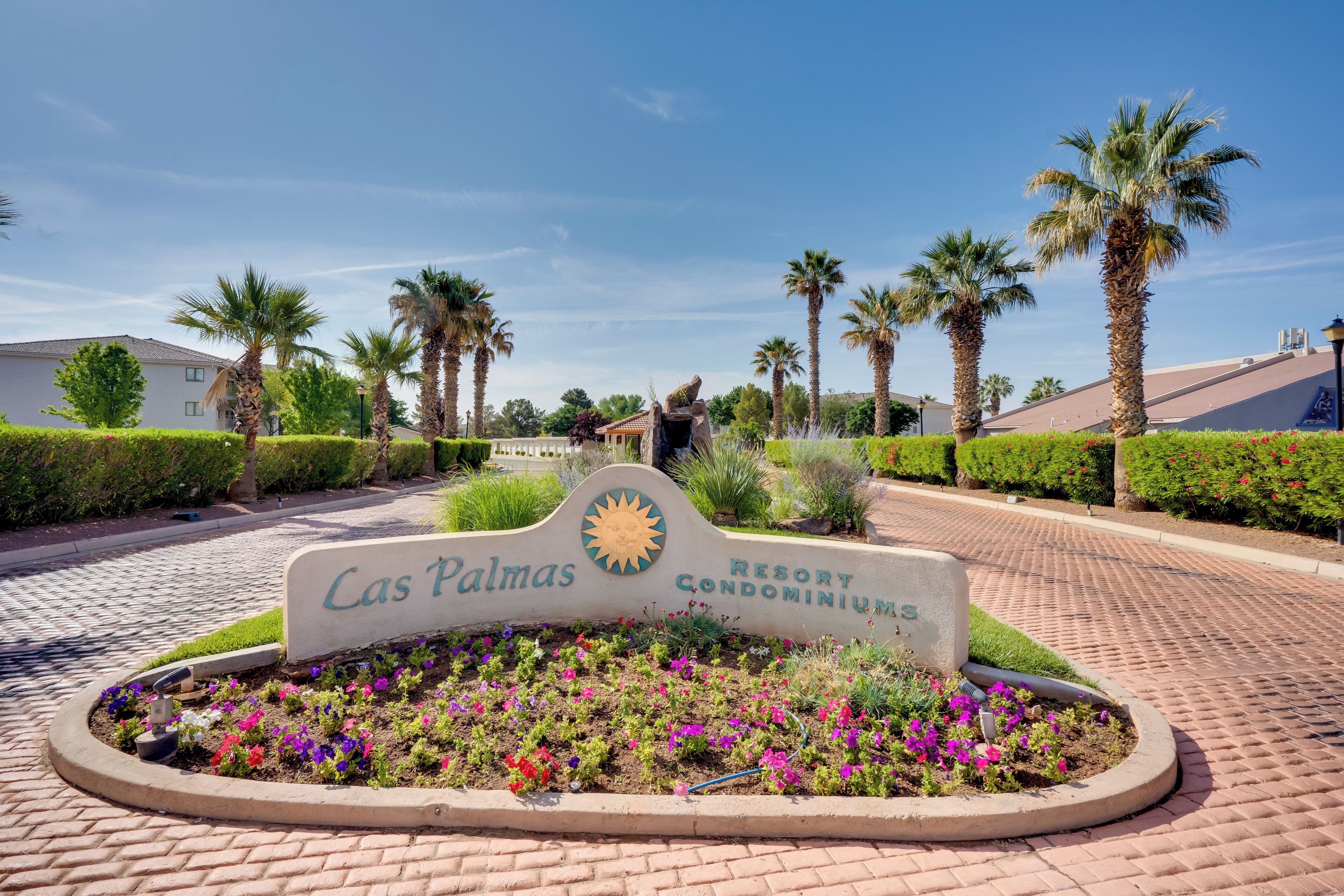 Schild für die Las Palmas Resort Condominiums, umgeben von einem angelegten Garten mit Palmen und Blumen.