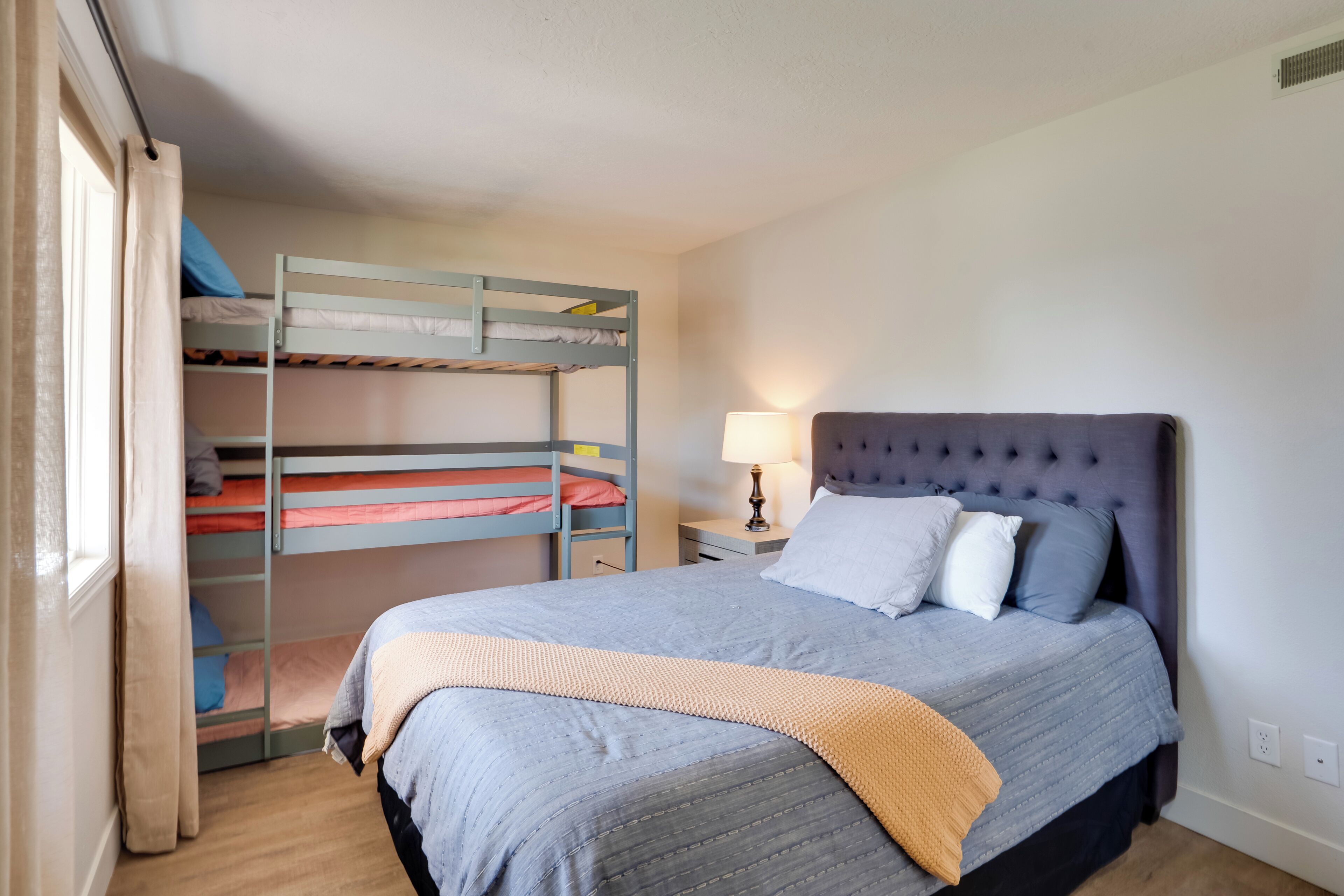 Ein Schlafzimmer mit einem Einzelbett, einem Etagenbett, einer Nachttischlampe und einem Fenster mit Vorhängen.
