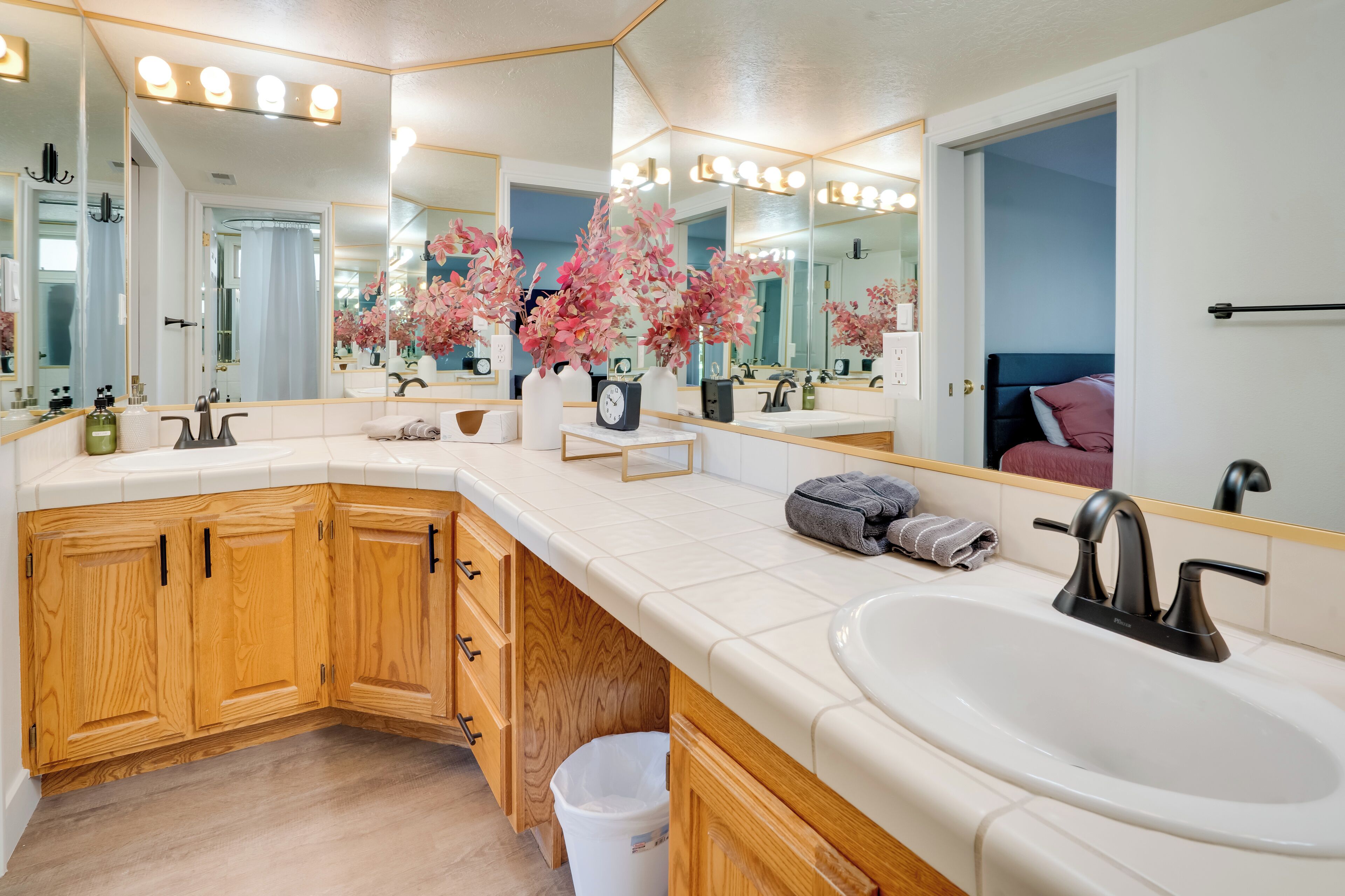 A modern bathroom with a large mirror, wooden cabinets, a white sink, and pink flowers on the countertop.