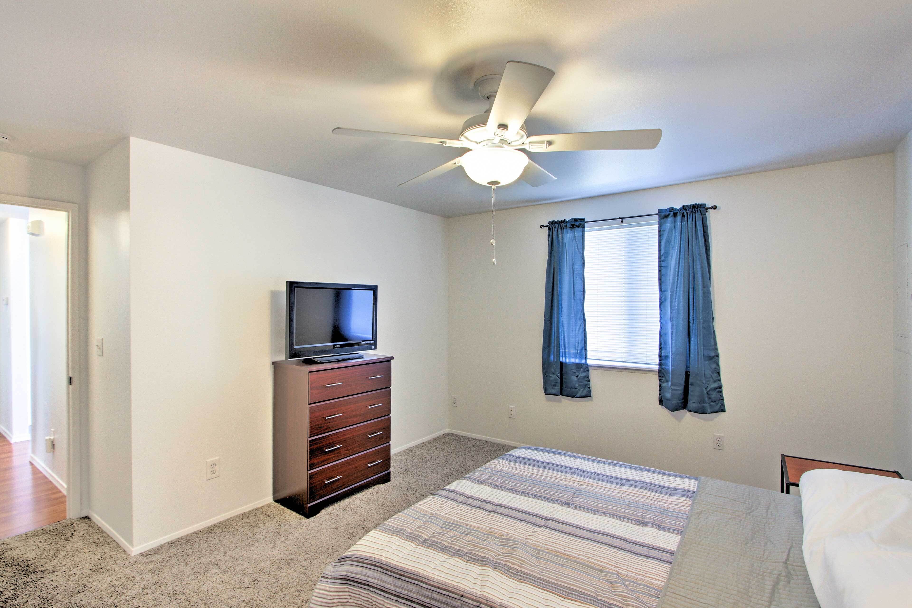 A bedroom with a bed, a dresser, a ceiling fan, and a window with curtains.