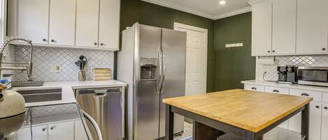 A modern kitchen with white cabinets, a stainless steel refrigerator, a wooden table, and a dishwasher.