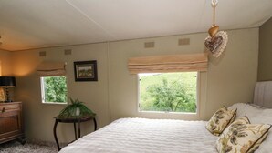 A bedroom with a large bed, two windows, a dresser, and a small table with a plant. - Gwybedog (Llanwrda)