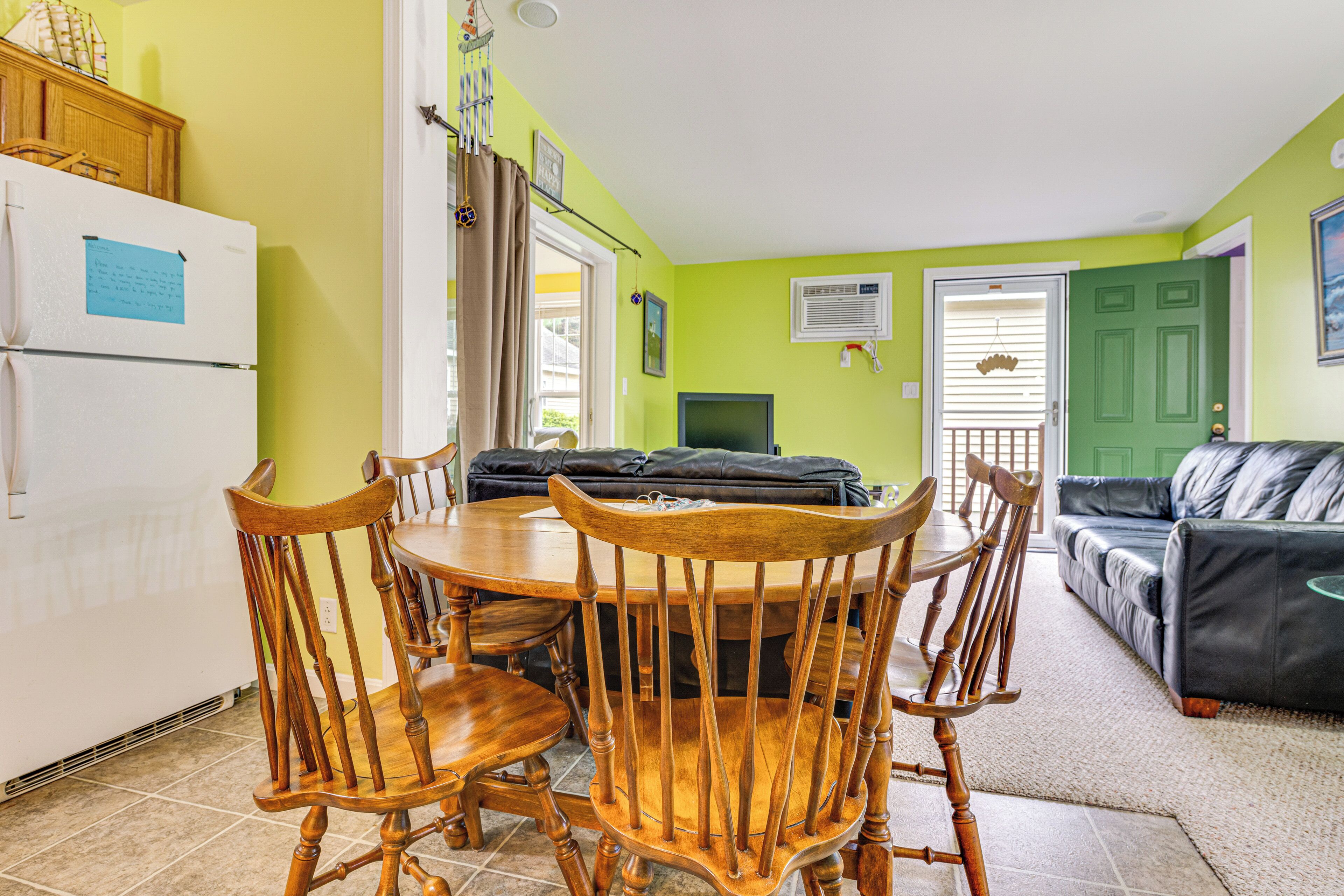 A dining area with a wooden table and chairs, a white refrigerator, and a green door in the background.