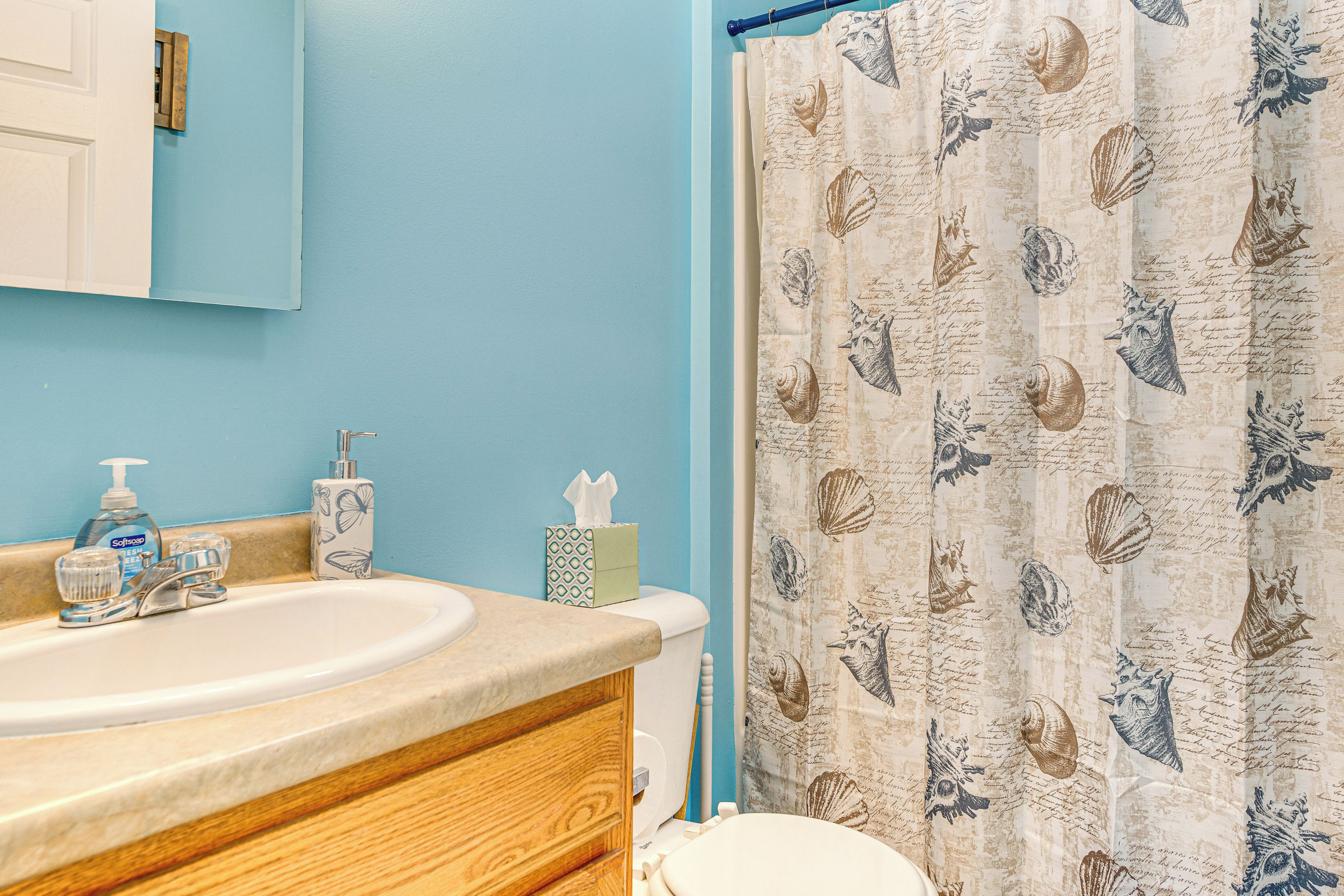 A bathroom with a sink, toilet, and shower curtain with a seashell pattern.