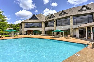 A large outdoor swimming pool with lounge chairs and umbrellas, surrounded by a building with large windows and stone pillars.