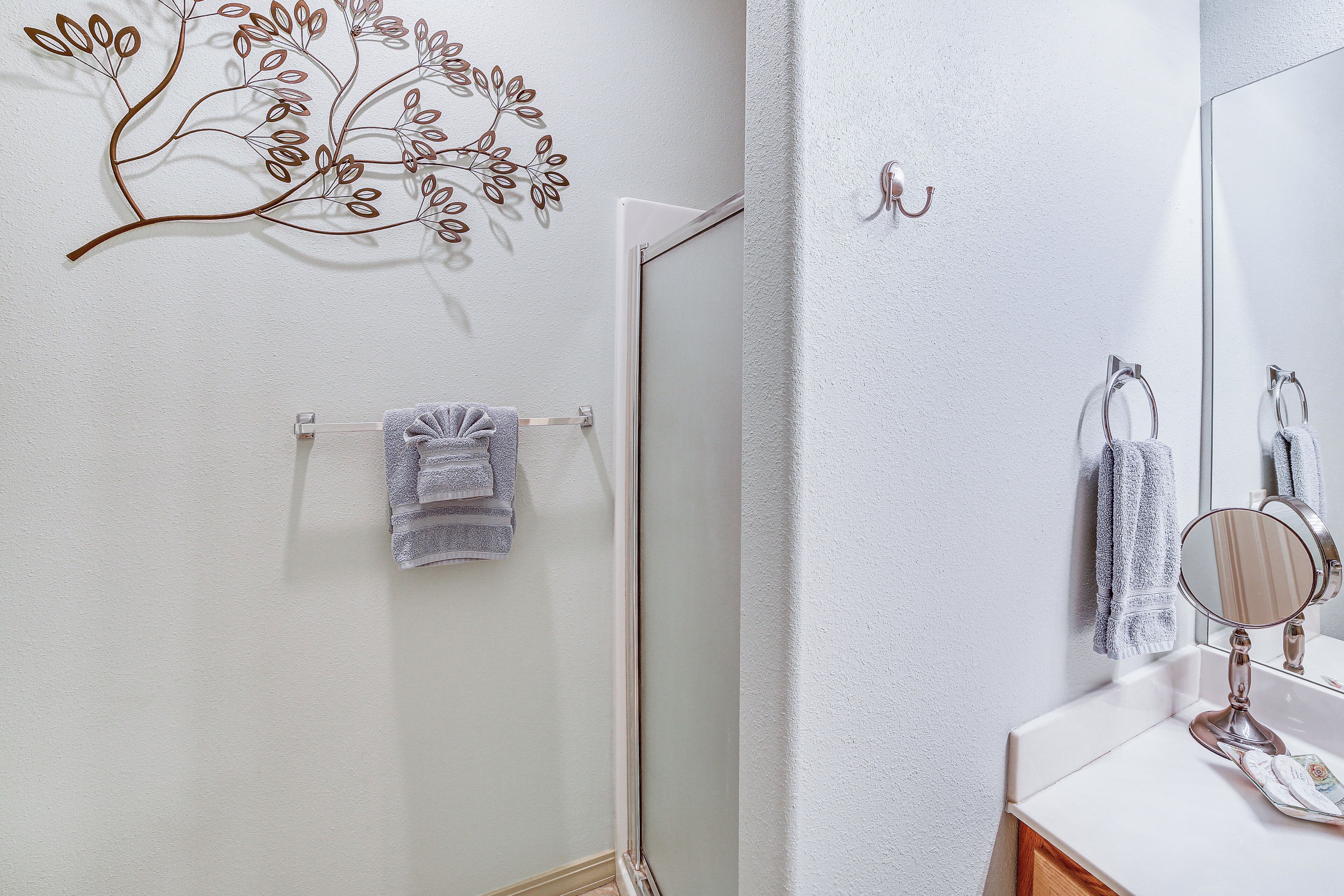 Een badkamer met een witte muur, een metalen wanddecoratie, een handdoekhouder met een handdoek, een spiegel en een douchedeur.