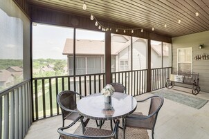 A covered patio with a round table and four chairs, a vase with flowers, and a view of neighboring houses.