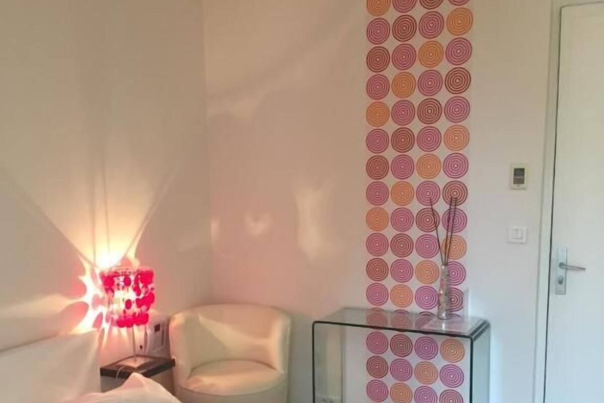 A modern bedroom with a bed, a chair, a bedside table, and a wall with circular patterns.
