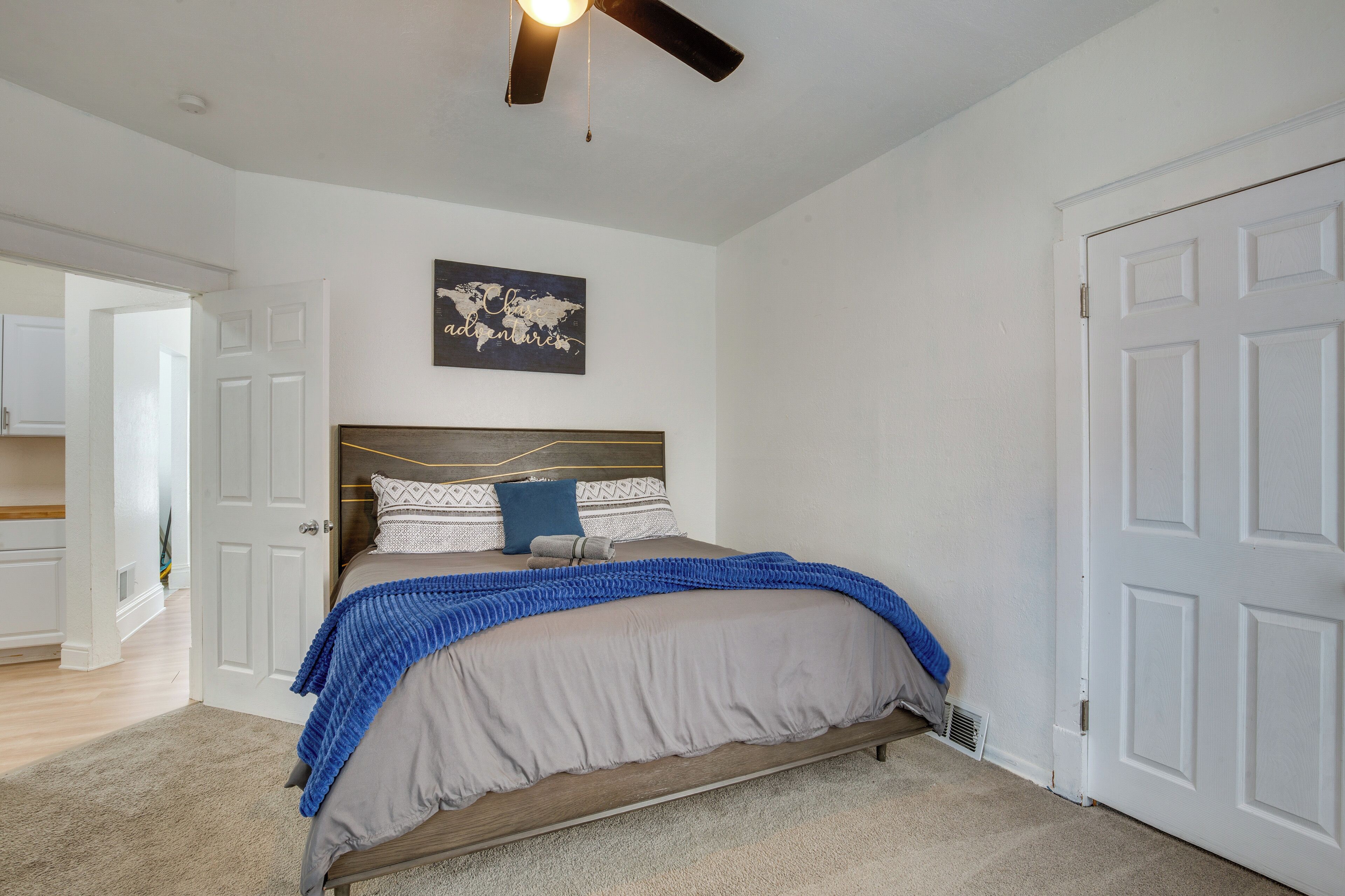 Une chambre à coucher avec un lit, un ventilateur de plafond, une décoration murale représentant une carte du monde et une porte blanche.