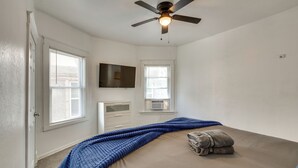 A bedroom with a bed, a ceiling fan, a TV mounted on the wall, and a window with blinds. - Modern 2BR Kansas City Condo Near Downtown (Kansas City)