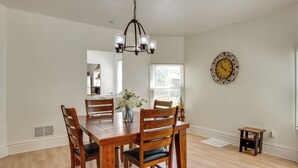 A dining room with a wooden table and chairs, a chandelier, a clock on the wall, and a window with blinds. - Modern 2BR Kansas City Condo Near Downtown (Kansas City)