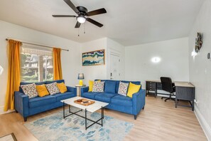 Ein Wohnzimmer mit einem blauen Sofa, einem Couchtisch und einem Schreibtisch mit einem Stuhl.
