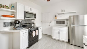 A modern kitchen with white cabinets, a stainless steel refrigerator, a microwave, a stove, and a ceiling fan. - Luxurious 2BR Kansas City Condo Near Downtown (Kansas City)