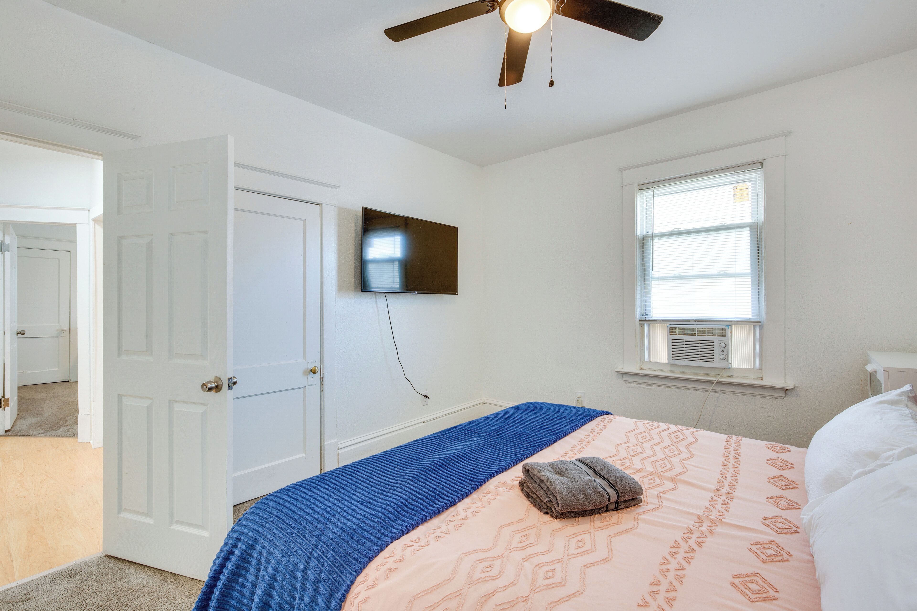 Ein Schlafzimmer mit einem Bett, einem Deckenventilator, einem an der Wand befestigten Fernseher und einem Fenster mit Jalousien.