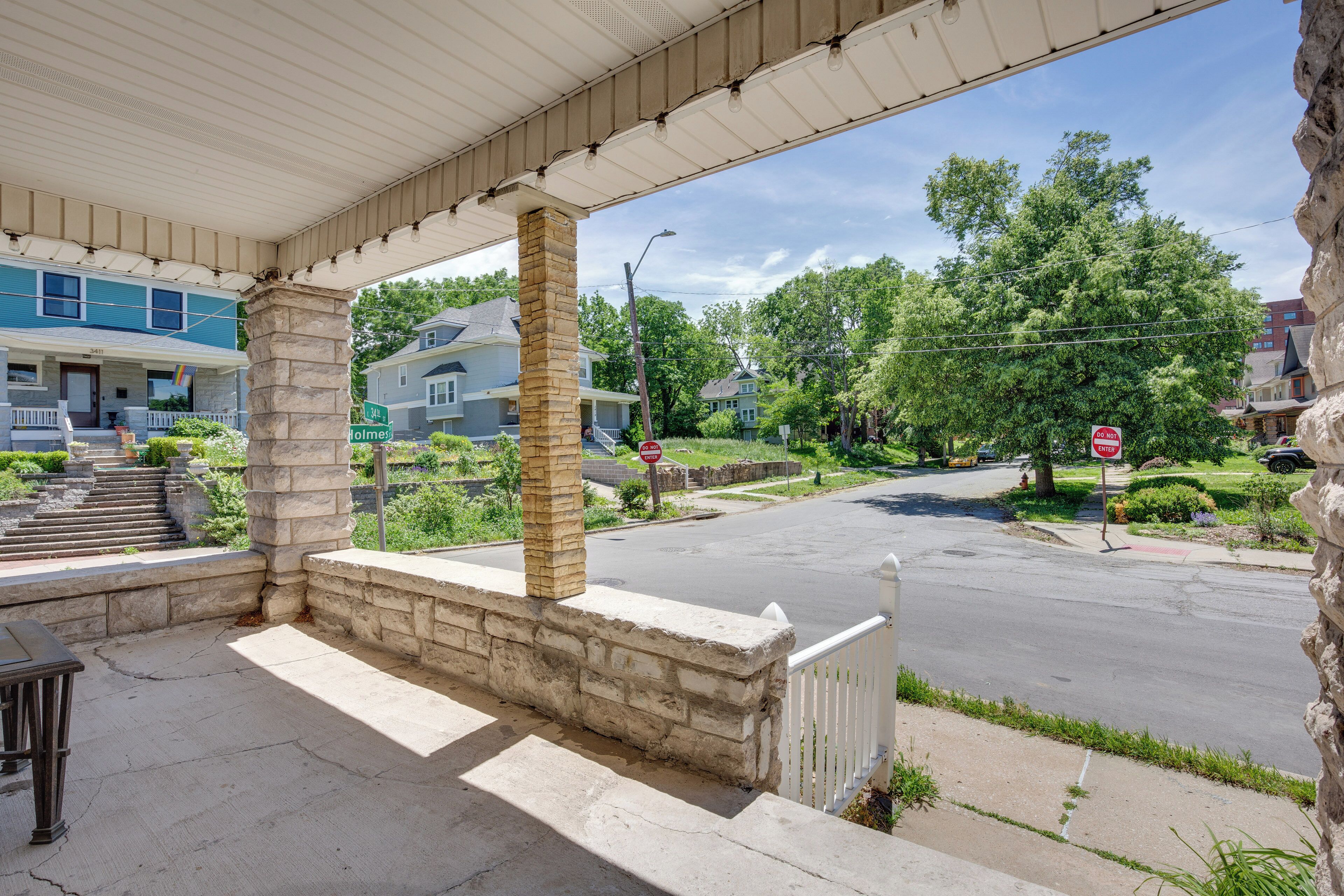 A covered outdoor area with a stone pillar, a white fence, and a view of a residential street.