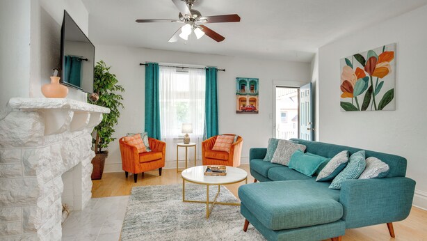A living room with a stone fireplace, teal sofa, orange armchairs, and a ceiling fan. - Luxurious 2BR Kansas City Condo Near Downtown (Kansas City)
