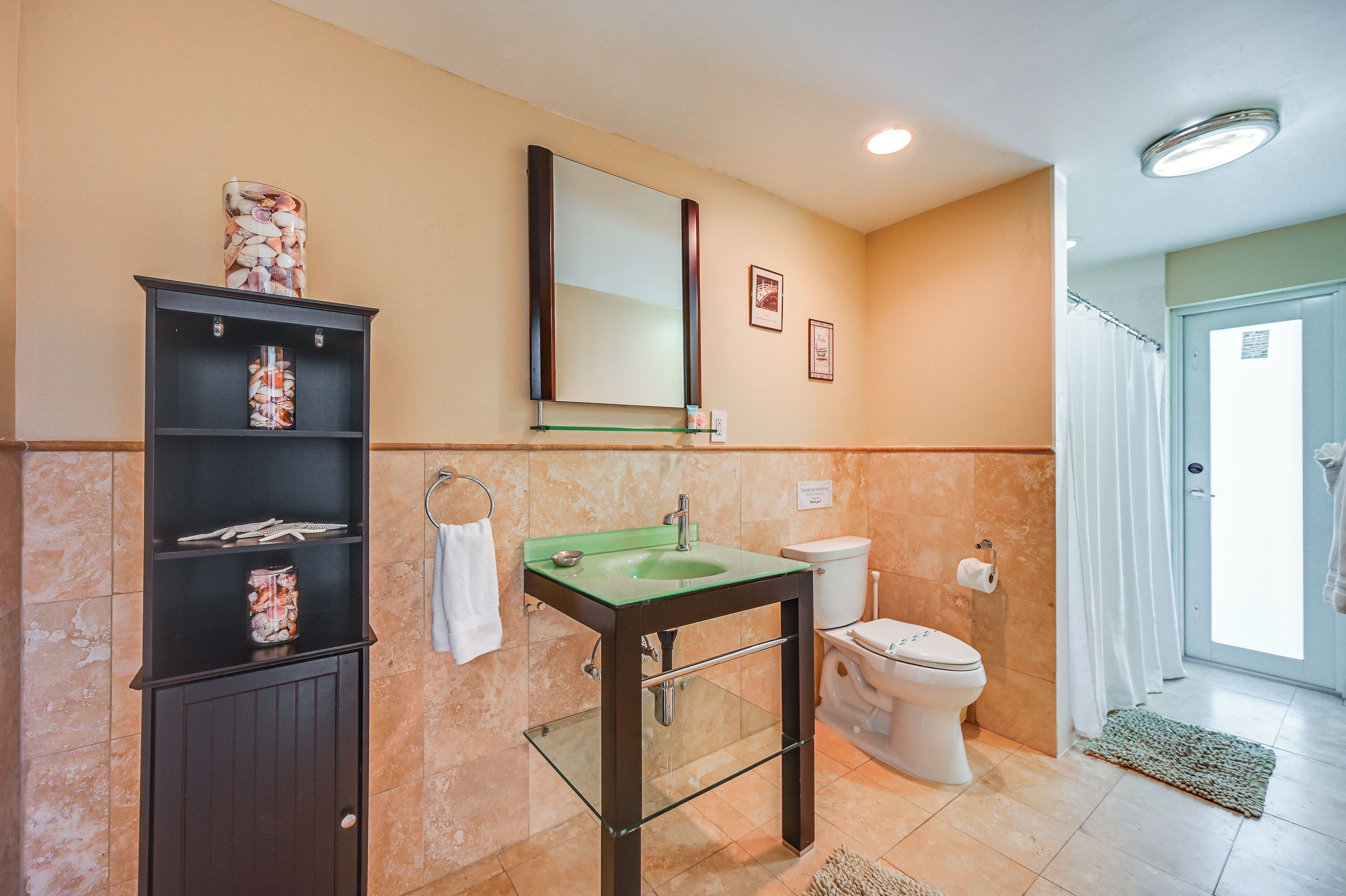 A bathroom with a glass sink, dark cabinet, toilet, and a shower area.