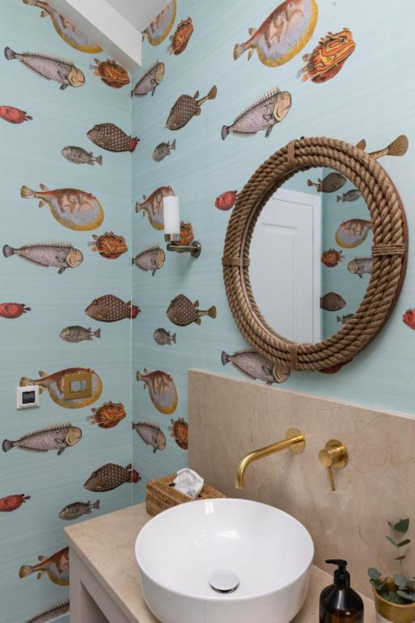 A bathroom with a sink, mirror, and fish-patterned wallpaper.