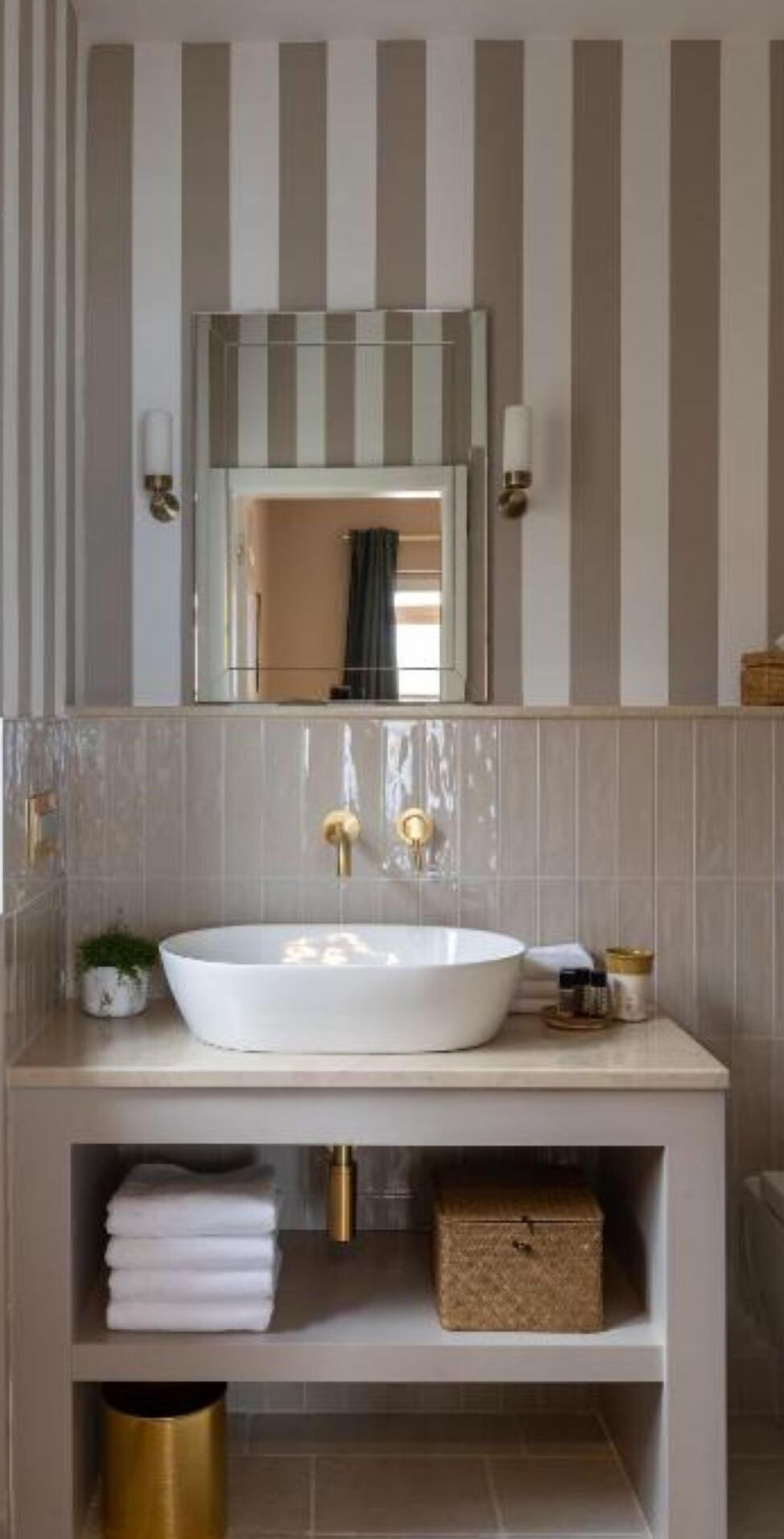 A bathroom with a large white sink, a mirror above it, and a striped wall. There are towels and a small plant on the counter.