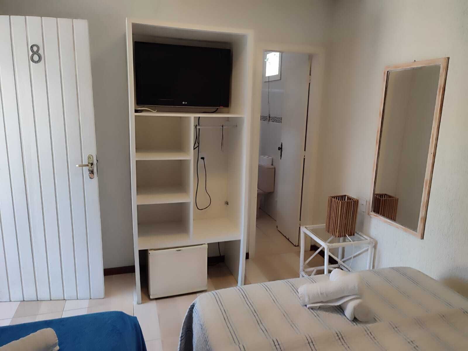 Un dormitorio con cama, televisor sobre un mueble bajo, armario y baño visible a través de una puerta abierta.