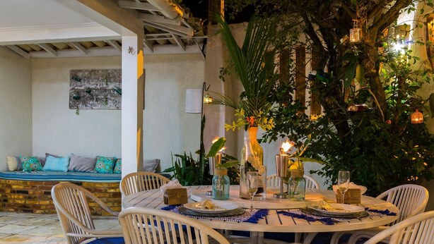 A round dining table with white chairs, surrounded by greenery and decorative lanterns. - Pousada Maresia Buzios (Buzios)
