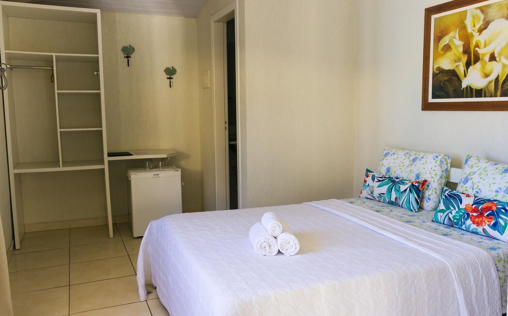 A hotel room with a bed, a small refrigerator, a closet, and a painting on the wall.
