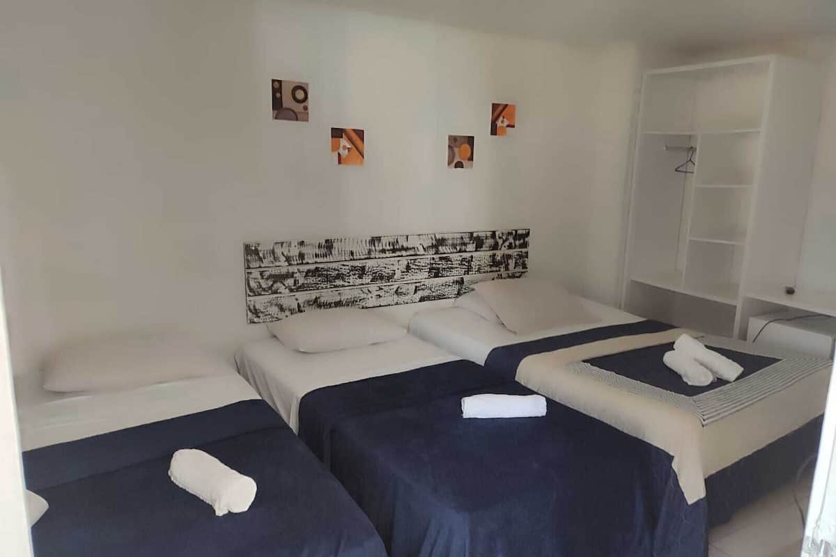Una habitación de hotel con dos camas individuales, una cama grande con cabecera y un armario.