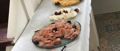 Una mesa de buffet con diferentes alimentos, incluyendo carnes, frutas y un vaso de jugo de naranja.