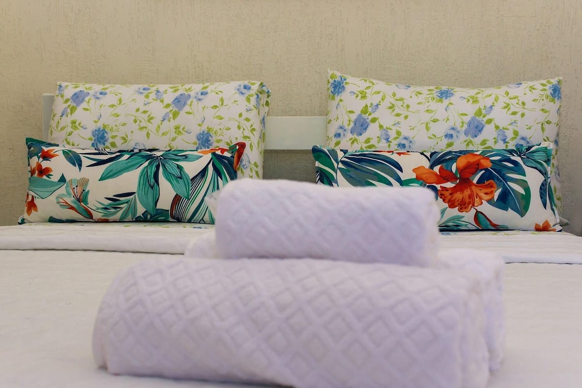 Una cama bien tendida con almohadas de estampado floral y una toalla blanca enrollada.