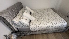 A small, compact bed with a grey headboard and white bedding with a leaf pattern. - Bright 2 bed maisonette flat in Romford (Romford)