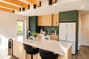 A modern kitchen with a central island, wooden cabinets, a refrigerator, and a built-in oven. - Spa & Lake | Orphee (Chertsey)