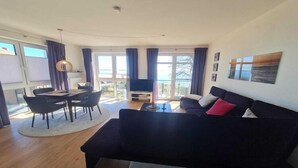 A modern living room with a black sofa, a dining table with chairs, and a TV. - Apartment in Orth (Orth)