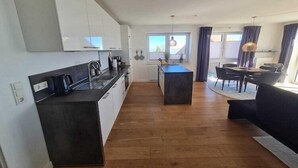 A modern kitchen with white cabinets, a central island, and a dining area with a table and chairs. - Apartment in Orth (Orth)
