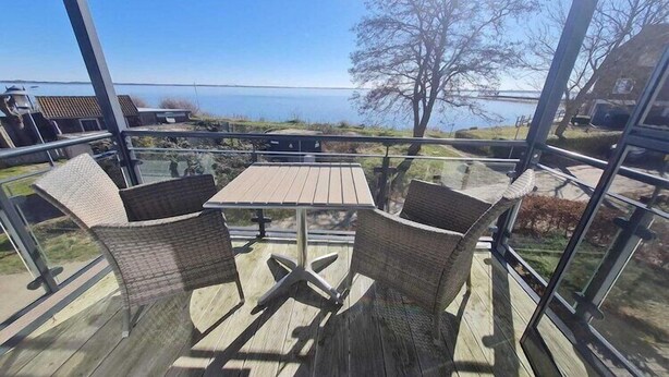 A wooden deck with a table and chairs, overlooking a body of water and a distant shoreline. - Apartment in Orth (Orth)