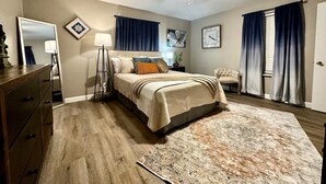 Une chambre à coucher avec un lit, une commode, un ventilateur de plafond, une horloge et une fenêtre avec des rideaux.