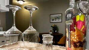 Un plateau contenant trois verres transparents, une bouteille de mélange pour préparer des cocktails à base de vodka et une passoire en métal, le tout posé sur une surface en bois.