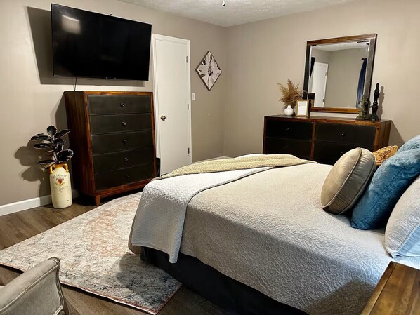 Une chambre à coucher avec un lit, une commode, une télévision et un miroir.