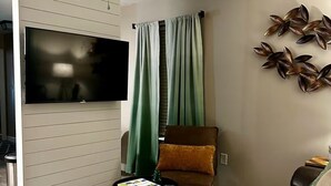 Un salon doté d’un ventilateur de plafond, d’un téléviseur à écran plat, d’un canapé en cuir marron, d’un fauteuil vert et d’une table basse avec des magazines.