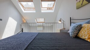 Un dormitorio con cama, mesita de noche, lámpara y tragaluces.