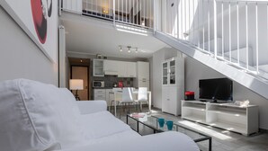Una sala de estar moderna con un sofá blanco, una mesa de centro y un televisor sobre un mueble blanco. Una escalera conduce a un nivel superior.