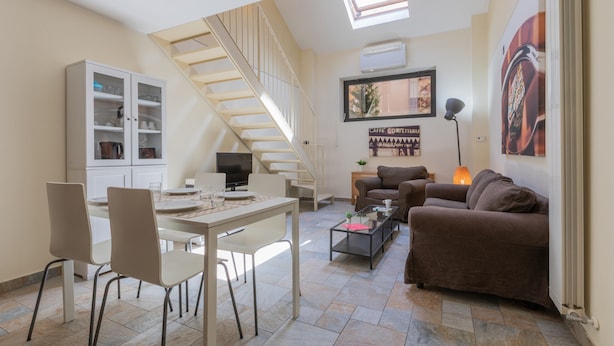 A modern living room with a dining area, a staircase, and a large window. - Loft Cioccolato by Wonderful Italy (Turin)