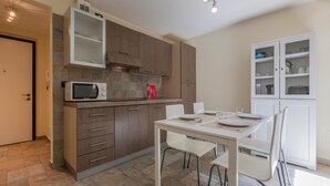 A modern kitchen with a microwave, stove, and cabinets. There is a dining table with chairs and a cabinet with glass doors. - Loft Cioccolato by Wonderful Italy (Turin)