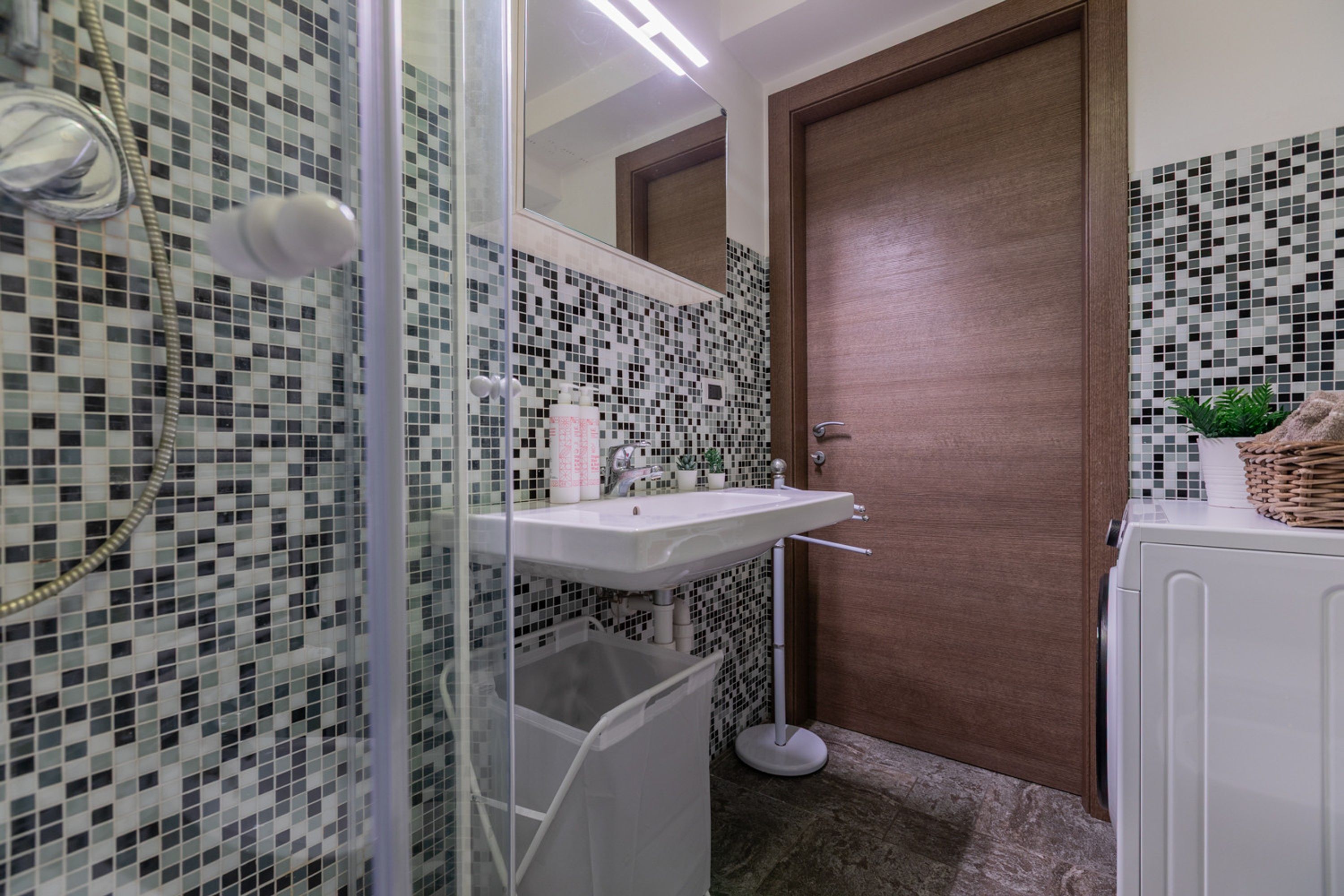 Un baño con cabina de ducha de vidrio, un lavabo blanco y pared con azulejos.