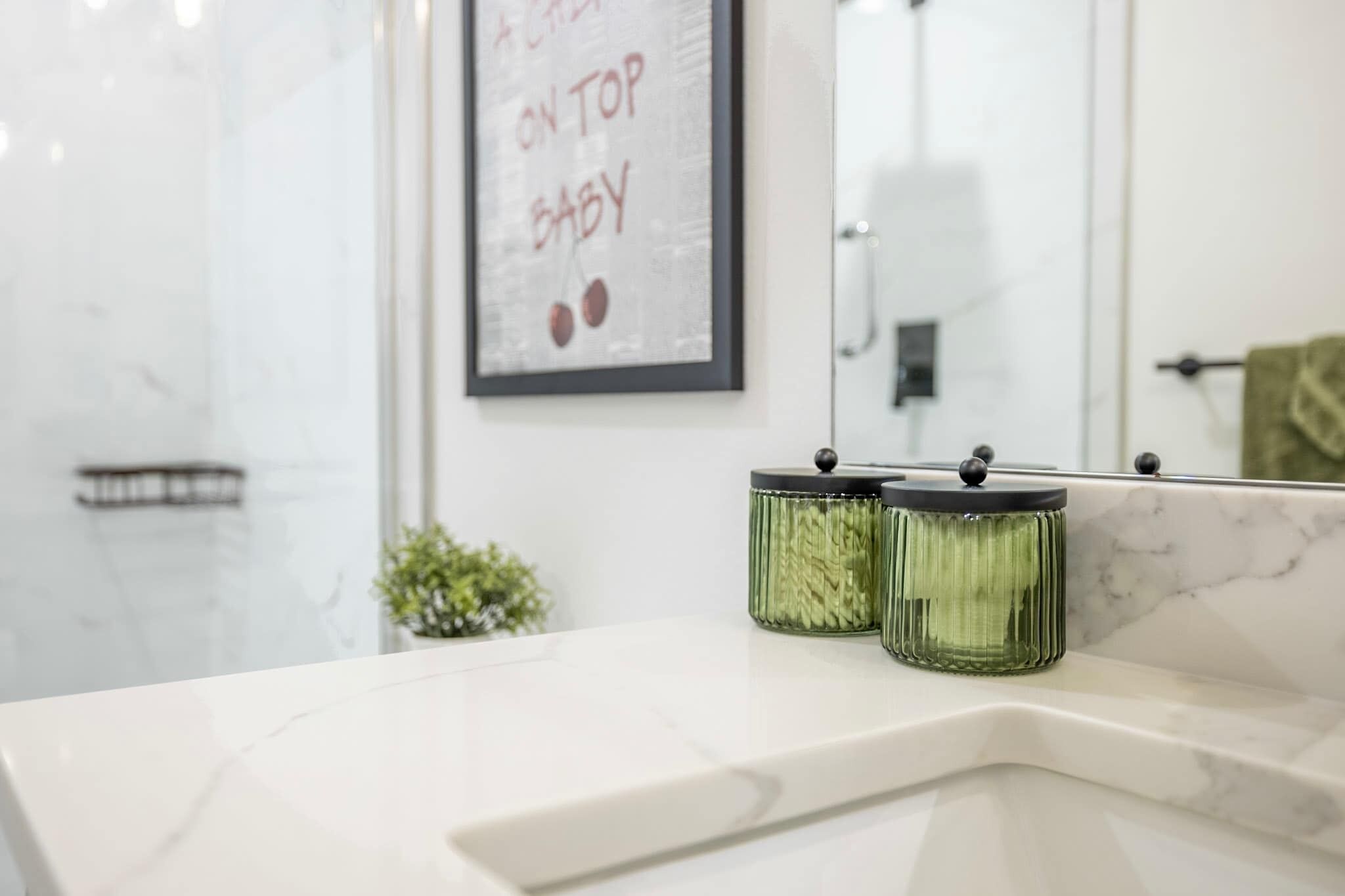 A bathroom with a white marble countertop, a framed picture on the wall, and two green glass jars on the counter.