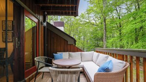 A covered outdoor seating area with wicker furniture and a cushioned sofa, overlooking a forested area. - Fall Foliage, Hiking Trails, Close to Jim Thorpe! (Lake Harmony)