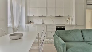 A modern kitchen with white cabinets, a dining table with a bowl, and a green sofa. - Elegant 2-bed apt in the Centre of Milan (Milan)