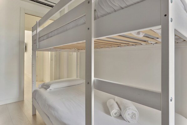 Habitación con literas en una paleta de colores blancos, una puerta que da a otra habitación y una toalla en la litera inferior.